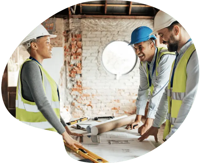 Three construction workers discussing plans at a worksite table.